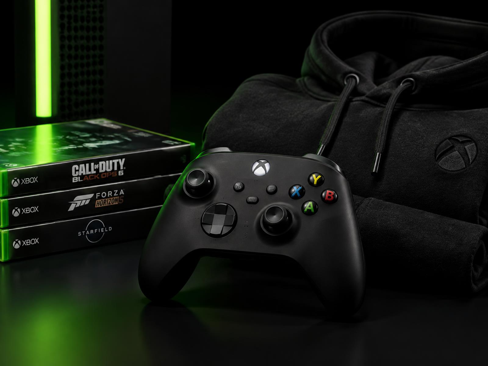 Console controller, game cases and a black hoodie on a dark studio surface